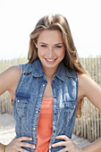 A young blonde woman on a beach wearing an orange top