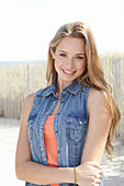 A young blonde woman on a beach wearing an orange top