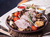 Slices of baked roasted meat. Cold-boiled pork with mushrooms, garlic and cherry tomato on brown plate