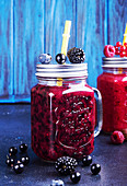 Summer smoothies of blackberries, blueberries, red and black currant, raspberries in glasses on blue background