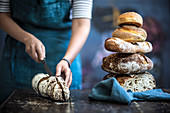 Frau halbiert Brotlaib neben gestapelten Broten auf Holztisch