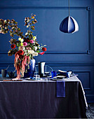 Laid table in shades of blue with a lush bouquet of flowers, pendant lights above
