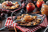 Bohemian Kaiserschmarrn with applesauce and roast plums in a cast-iron pan on a red and white cloth