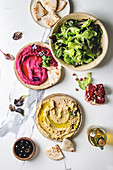 Variety of homemade traditional and beetroot spread hummus with pine nuts, olive oil, pomegranate served on ceramic plates with pita bread and green salad