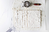 Homemade honey nuts nougat turron sliced on crumpled paper with vintage sieve and sugar powder over white marble background