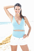 A brunette woman on a beach wearing a light-blue bathing suit and white shorts