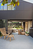 Rattan chair on concrete terrace with roofed dining area in background