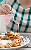 A woman drizzling icing onto a plate of cinnamon buns, with a glass of sparkling pink lemonade in the background