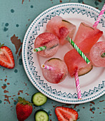 Gin and tonic popsicles with strawberries and cucumbers on a mint coloured tray
