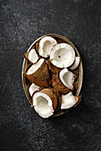 Cracked coconuts arranged in metallic tray on dark background
