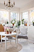 Round table, armchair, wooden bench and houseplants in Scandinavian-style conservatory