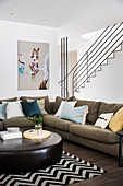 Gemütliche Sofagarnitur mit Kissen und Leder-Couchtisch vor Treppe im Wohnzimmer