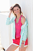 A young woman on a beach wearing a pink top, a jacket and shorts