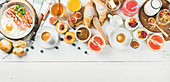 Fried egg with sausages and bacon, bread, croissants, jam, fruit, smoothie, juice, yogurt, granola with milk and coffee on white wooden background