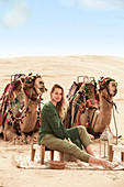 Junge Frau in grüner Tunika und Hose in der Wüste mit zwei Kamelen