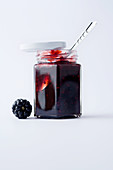 A glass of blackberry jam against a white background