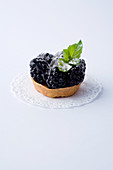 A mini tartlet with blackberries against a white background