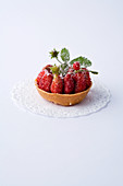 A mini tartlet with wild strawberries against a white background