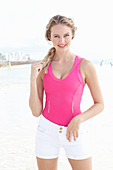 A blonde woman on a beach wearing a pink top and light shorts