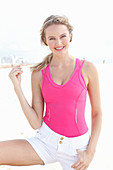 A blonde woman on a beach wearing a pink top and light shorts