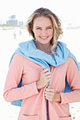 A blonde woman wearing an apricot cardigan with a jumper over her shoulders