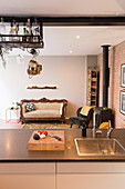 Blick über Küchentheke auf Kaminofen, Retro Sessel, Holzlager und Sofa in offenem Wohnraum mit Ziegelwand