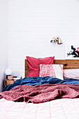 Wooden bed with cozy bed linen in red and blue against a white wall