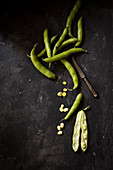 Broad beans on a black surface with an old knife