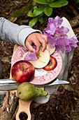 A little child hand picking a flower from a plate with a apple and a pear