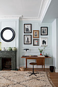 Teakholz-Schreibtisch neben Marmor-Kamin, Fotogalerie und runder Spiegel an mintfarbener Wand