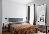 Double bed, jade-green pendant lamps above side tables and full-length mirror leaning against wall in bedroom