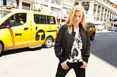 A blonde woman wearing a printed t-shirt, a jacket and black jeans
