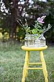 Garden flowers in apothecary bottles on yellow stool