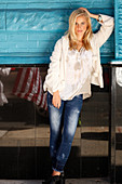 Junge blonde Frau in Tunikabluse, weißer Jacke und Jeans