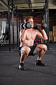 A young man performing a man maker big with dumbbells and a thruster
