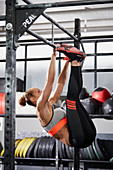 A young woman performing toes to bar windscreen wiper on a pull-up bar