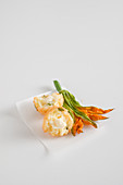 Frittiertes Reisbällchen mit Mozzarellafüllung und Zucchiniblüte auf weißem Papier
