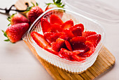 Close-up of plastic container filled with cream and sliced red strawberry