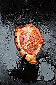 A grilled pork chop on a dark surface