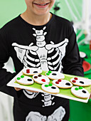 Child in skeleton costume holding ghost biscuits for Halloween