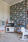 Play kitchen, shelves and rocking horse in child's bedroom with colourful wallpaper