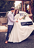 A bride and groom in front of a classic car