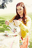Junge Frau mit Teekanne am Gartentisch