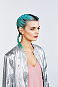 A young woman with blue hair wearing a pink top and a silver jacket