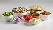Greek pitta bread surrounded by various ingredients in bowls