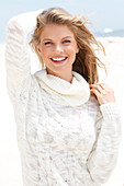 A blonde woman wearing a white rollneck jumper on the beach