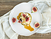 Marrow pancakes with fresh figs, honey and goat cheese on a white ceramic plate over a wood background