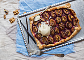Rustic plum pie with walnuts and ice-cream on a silver tray over pieces of linen fabric