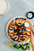 A woman sifting powdered sugar on a peach cake with blueberries