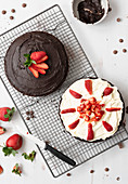 Preparation of chocolate dessert cake: one half spread with chocolate icing and the other covered in cream and cut strawberries